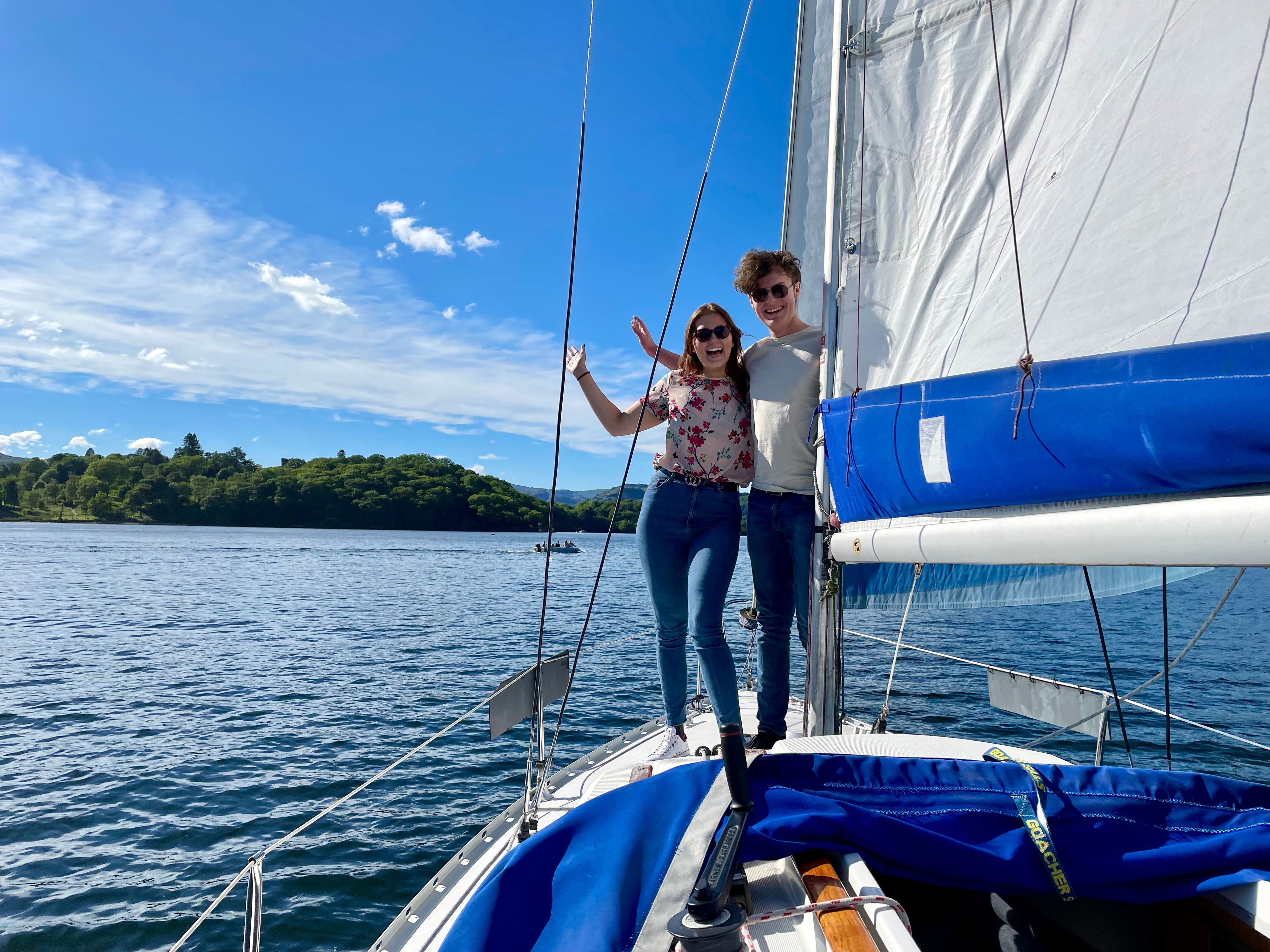 A man and woman are standing on a boat sailing across the lake.