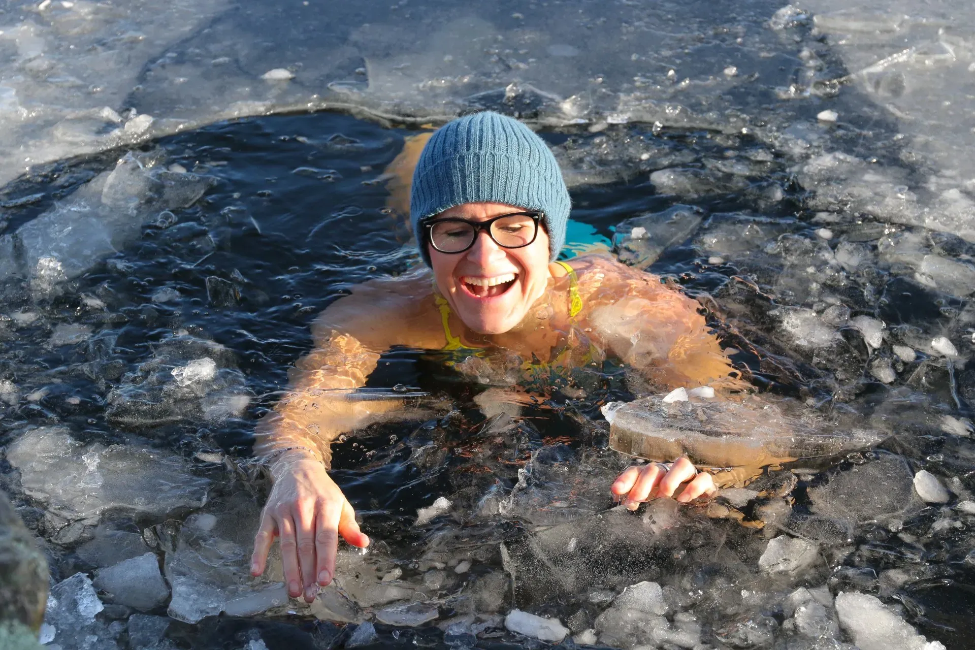 person in a lake filled with ice wearing glasses and a toque