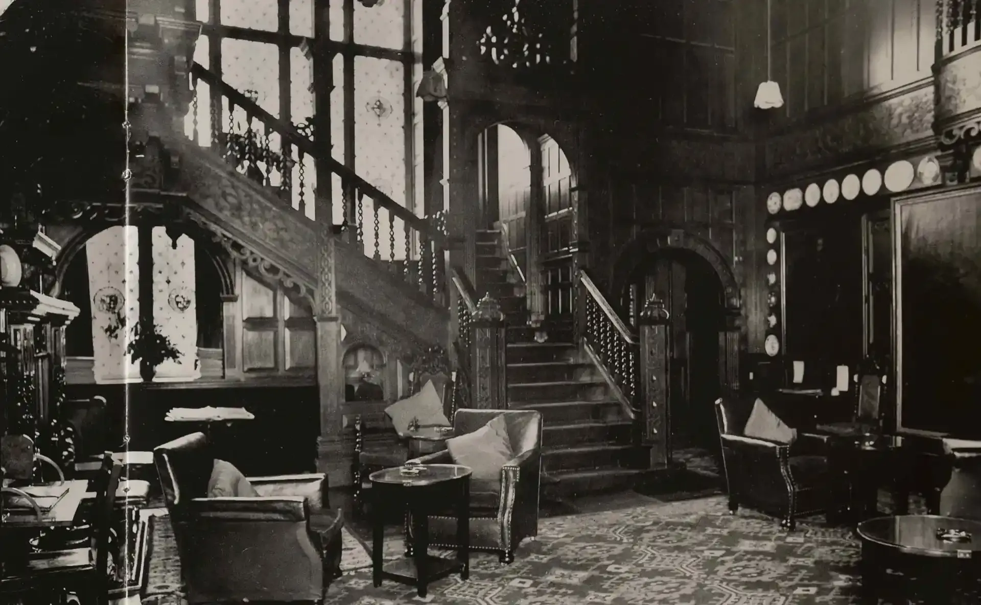 black and white photo of a Victorian-era hotel lobby with a staircase